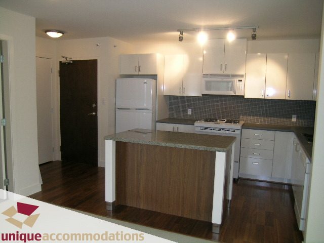 Bright kitchen with white cabinets, dark tiled backsplash, and hardwood floors. - 108 - 175 West 1st Street, North Vancouver