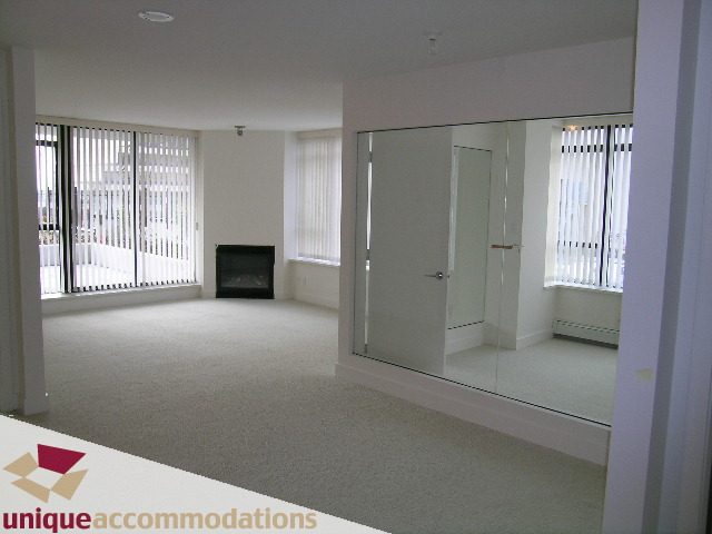 Spacious living room with large windows, neutral carpet, and mirrored closet doors. - 108 - 175 West 1st Street, North Vancouver