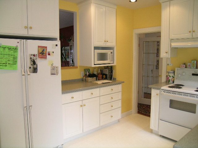 Bright kitchen with white cabinets, yellow walls, and a white refrigerator. - 2679 Ottawa Ave, West Vancouver