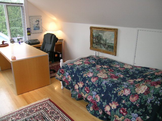Spacious bedroom with hardwood floors, floral bedding, and a desk area, perfect for a cozy stay. - 2679 Ottawa Ave, West Vancouver