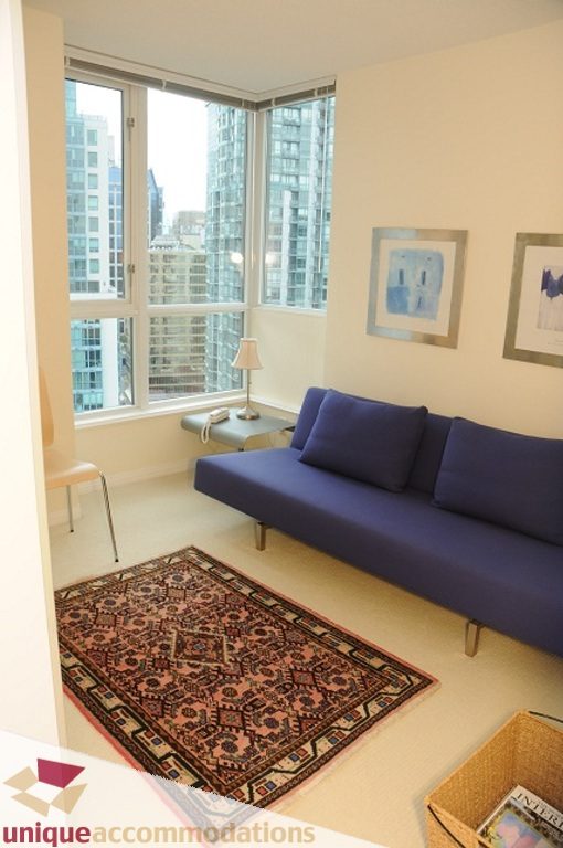Spacious living room with a cozy corner sofa, large windows offering a stunning city view, and a patterned rug adding warmth.