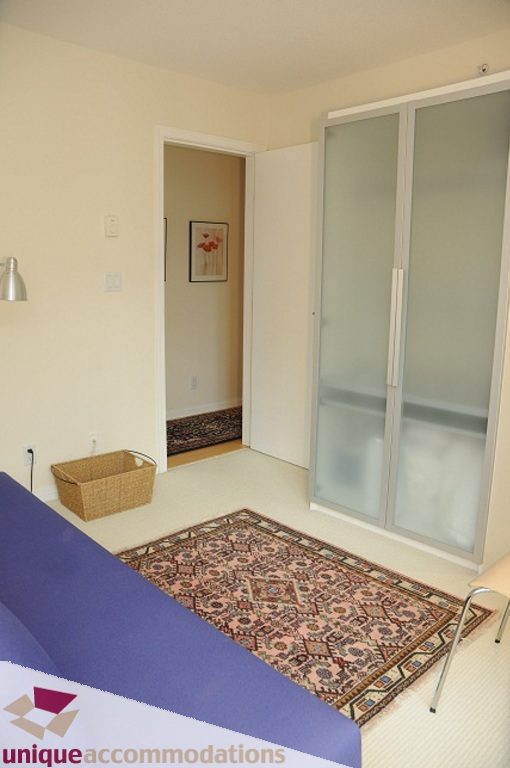 Spacious 1-bedroom + den with a cozy corner featuring a patterned rug and a sliding glass door leading to a private balcony.