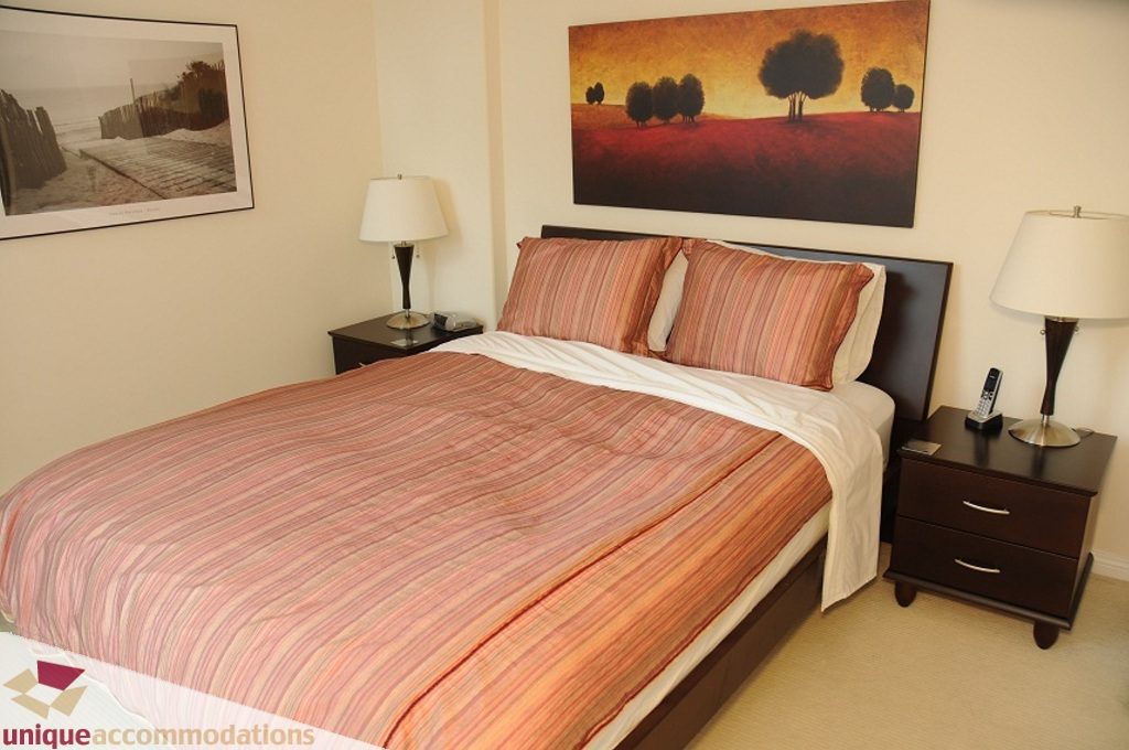 Spacious 1-bedroom + den condo with cozy striped bedding and modern artwork, perfect for downtown Vancouver living.