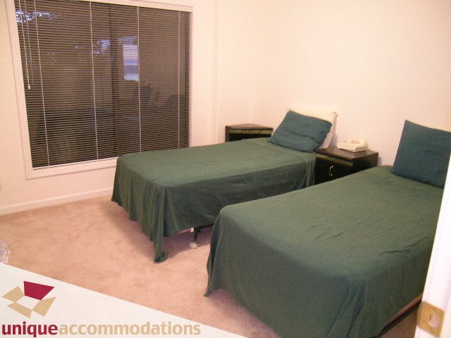 Furnished bedroom with two single beds, green bedding, nightstand, and window blinds. - 1416 Chartwell Drive, West Vancouver