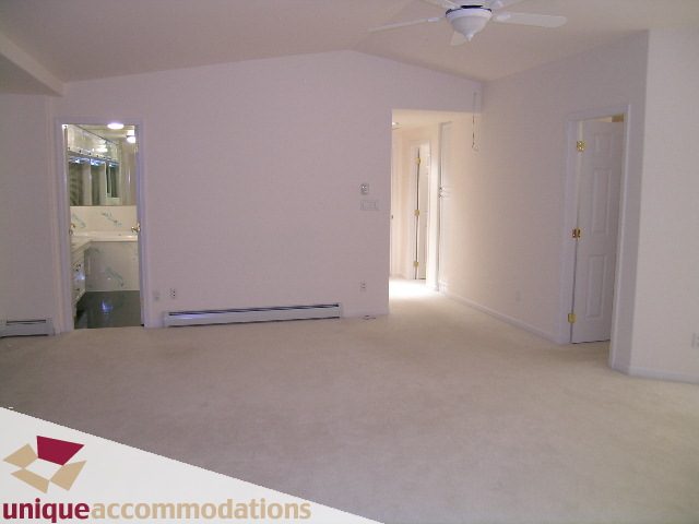 Bright living room with carpeted floors and white walls, leading to a hallway with double doors. - 1416 Chartwell Drive, West Vancouver