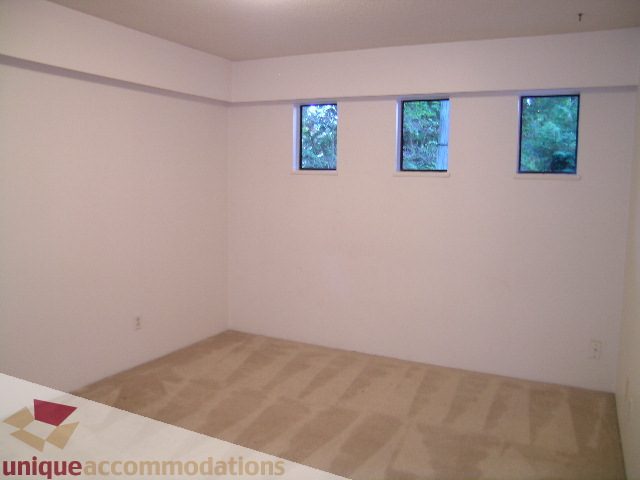 Bright bedroom with three windows showing greenery, carpeted floor. - 4655 Clovelly Walk, West Vancouver