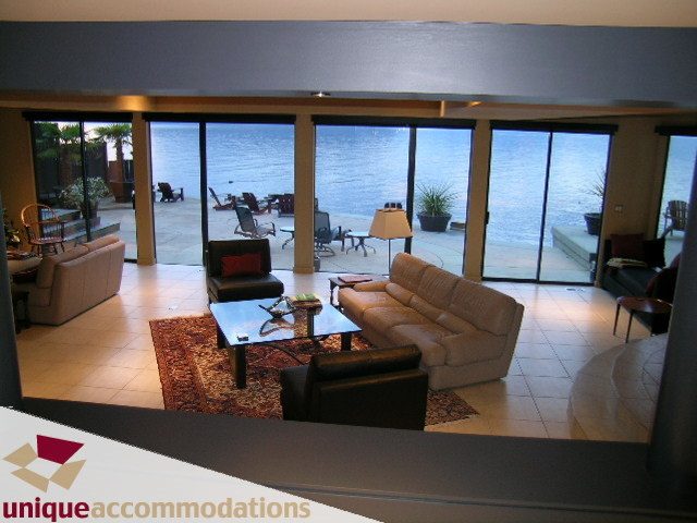 Spacious living room with large windows overlooking the water, featuring comfortable seating and a cozy fireplace.