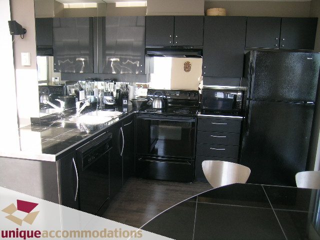 Bright kitchen with sleek black countertops, modern appliances, and hardwood floors. - 2001 - 1238 Richards Street, Vancouver Downtown