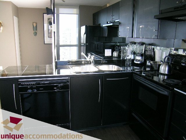 Bright kitchen with sleek black countertops and modern appliances, featuring a city view through large windows.