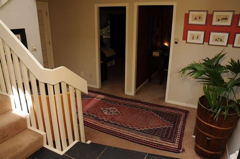 Foyer with patterned rug, wooden barrel planter, and white banister leading to stairs. - Guest House - 440 Stevens Drive, West Vancouver