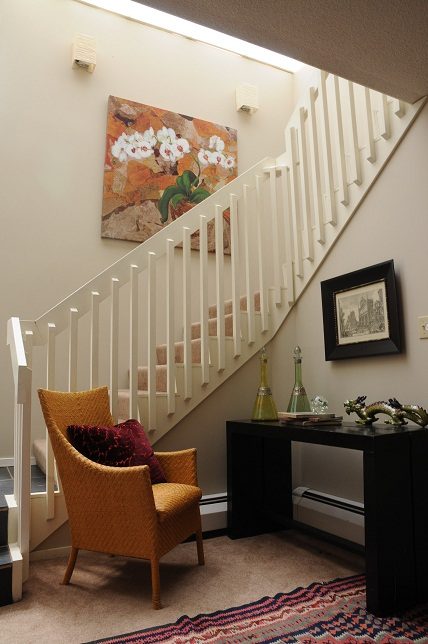Staircase landing with floral artwork, mustard chair, and black console table. - Guest House - 440 Stevens Drive, West Vancouver
