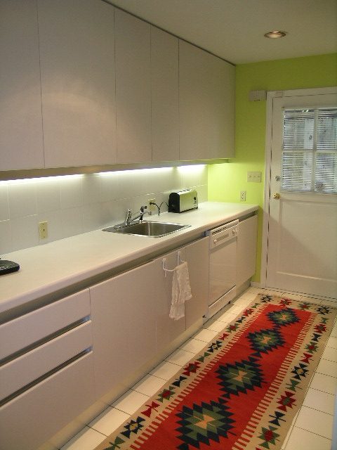 Bright kitchen with white cabinets, green accent wall, and colorful rug. - Guest House - 440 Stevens Drive, West Vancouver