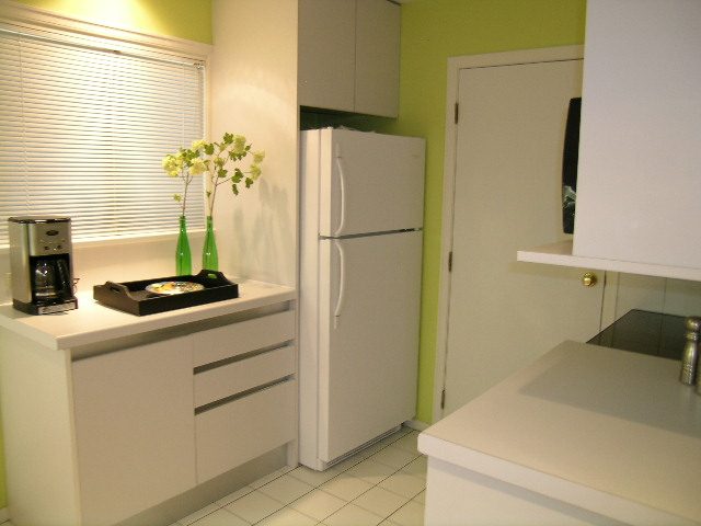 Bright kitchen with white countertops and a green accent wall, featuring a coffee maker and a vase with flowers.