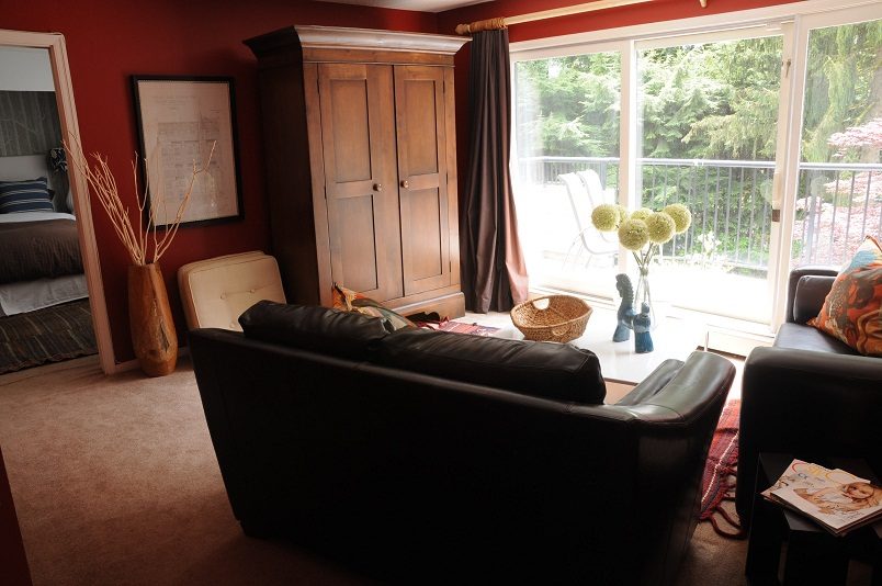 Bright living room with a large armoire, leather couch, and sliding glass door leading to a balcony. - Guest House - 440 Stevens Drive, West Vancouver