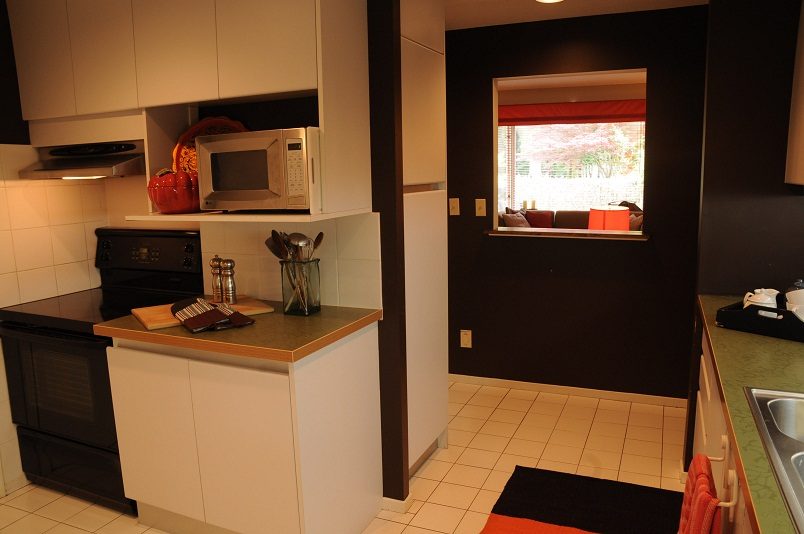 Bright kitchen with white cabinets, black countertops, and a window with red curtains. - Guest House - 440 Stevens Drive, West Vancouver