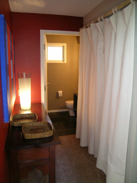 Guest bathroom with dark wood vanity, white shower curtain, and red accent wall. - Guest House - 440 Stevens Drive, West Vancouver