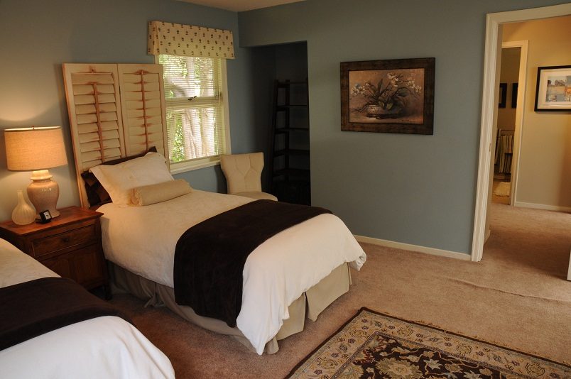 Cozy guest bedroom with a queen bed, wooden shutters, and a framed floral painting. - Guest House - 440 Stevens Drive, West Vancouver