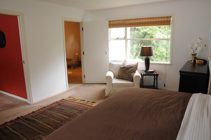 Bright bedroom with white walls, a cozy armchair, and a window with bamboo blinds. - Guest House - 440 Stevens Drive, West Vancouver