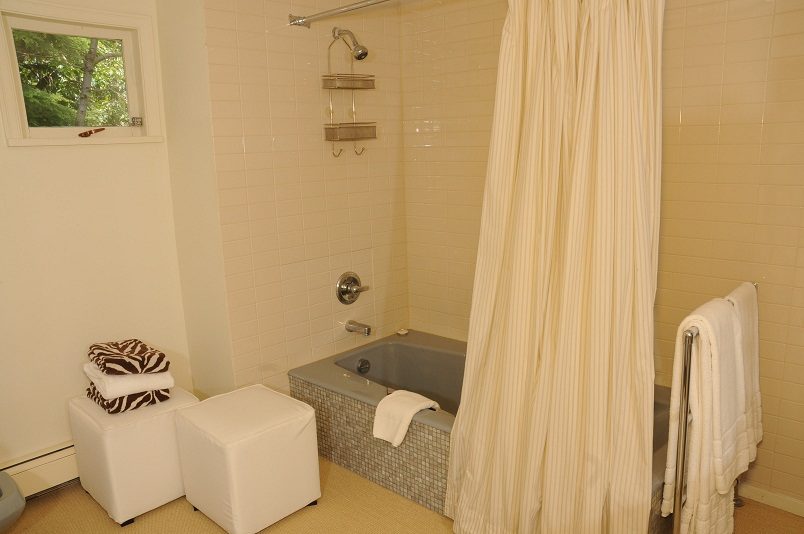 Bright bathroom with a bathtub, shower, and neatly folded towels. - Guest House - 440 Stevens Drive, West Vancouver