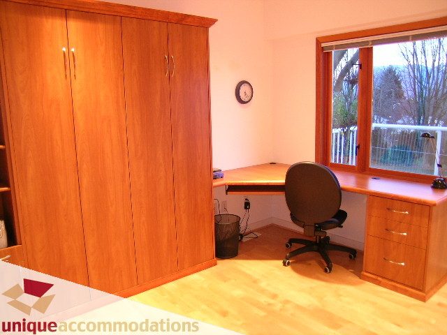 Furnished bedroom with wooden wardrobe, desk, and city view through sliding glass doors. - 3967 West Broadway, Vancouver West Side