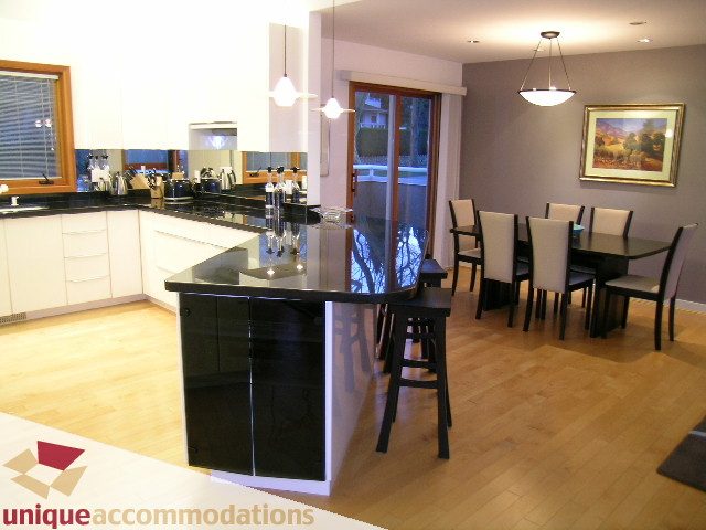 Modern kitchen with black countertops, hardwood floors, and a dining area with chairs. - 3967 West Broadway, Vancouver West Side