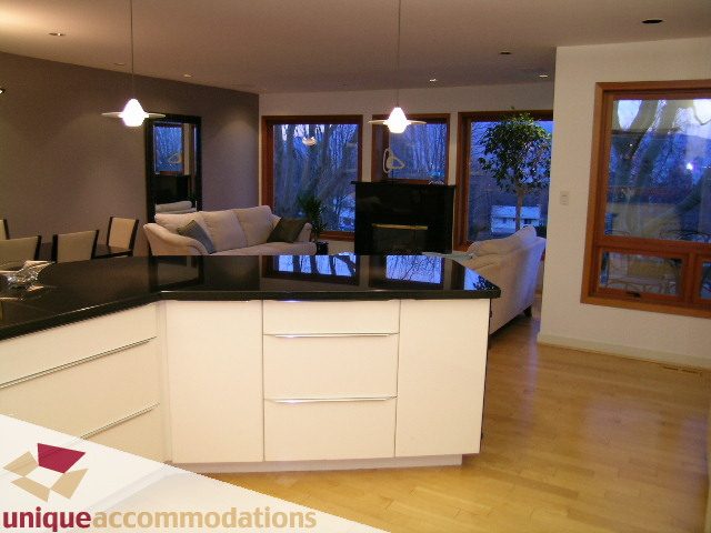 Furnished living room with hardwood floors and large windows, showcasing a cozy setup with a TV and comfortable seating.