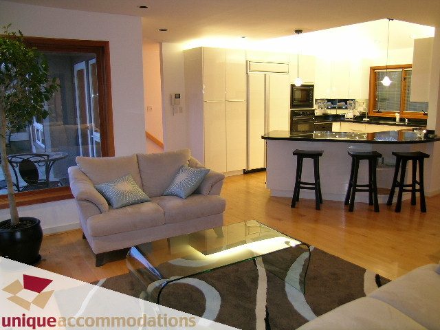Open-concept living and kitchen area with modern furnishings, hardwood floors, and a city view. - 3967 West Broadway, Vancouver West Side