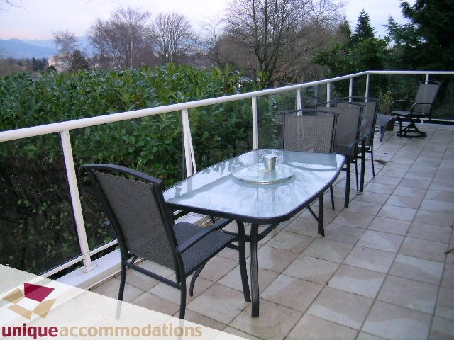 Furnished patio with glass-topped table and chairs, surrounded by greenery and trees. - 3967 West Broadway, Vancouver West Side