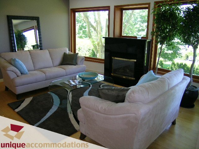 Furnished living room with large windows, hardwood floors, and a cozy fireplace. - 3967 West Broadway, Vancouver West Side