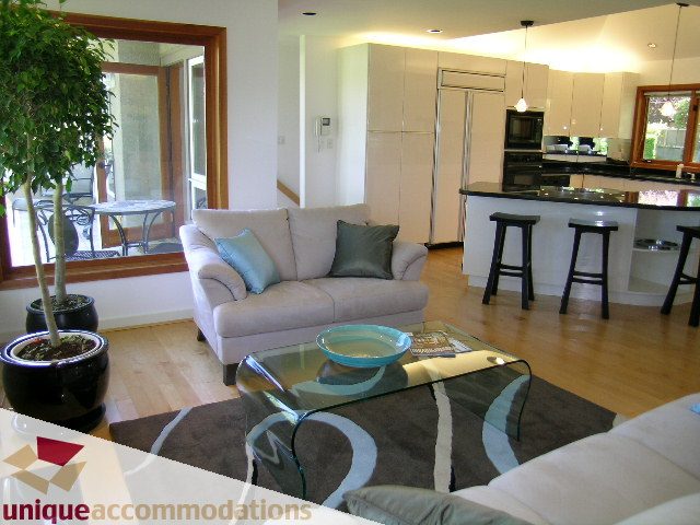 Open-concept living space with modern furnishings, hardwood floors, and a kitchen island. - 3967 West Broadway, Vancouver West Side