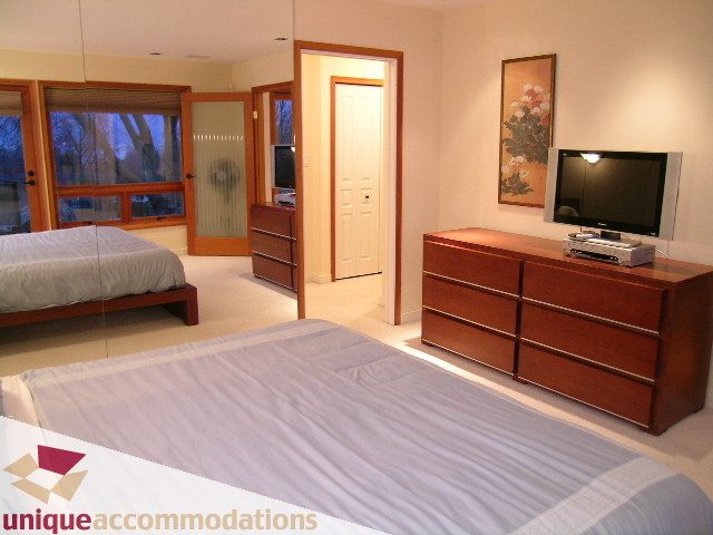 Spacious bedroom with wooden furniture, large bed, and sliding glass door leading to balcony. - 3967 West Broadway, Vancouver West Side