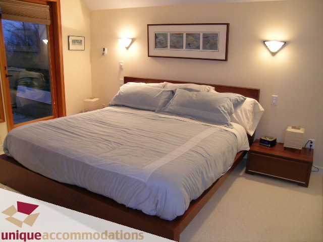 Spacious bedroom with wooden platform bed, white bedding, and wall sconces. - 3967 West Broadway, Vancouver West Side