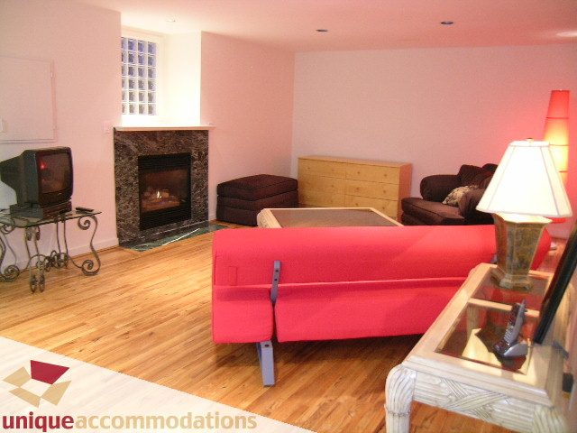 Bright living room with hardwood floors, a red sofa, and a fireplace. - 3967 West Broadway, Vancouver West Side