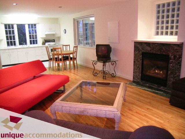 Furnished living room with hardwood floors, red sofa, and fireplace. - 3967 West Broadway, Vancouver West Side