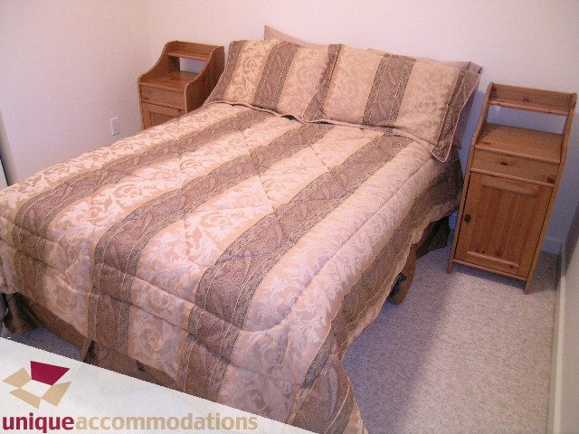 Furnished bedroom with wooden furniture and patterned bedding. - 3967 West Broadway, Vancouver West Side