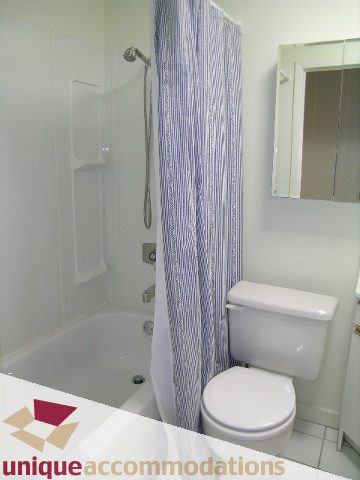 Furnished bathroom with white fixtures and striped shower curtain. - 3967 West Broadway, Vancouver West Side