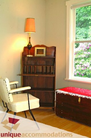 Bright sitting area with vintage chair, wooden bookcase, and window view of greenery. - 1 - 2812 Yukon, Vancouver West Side