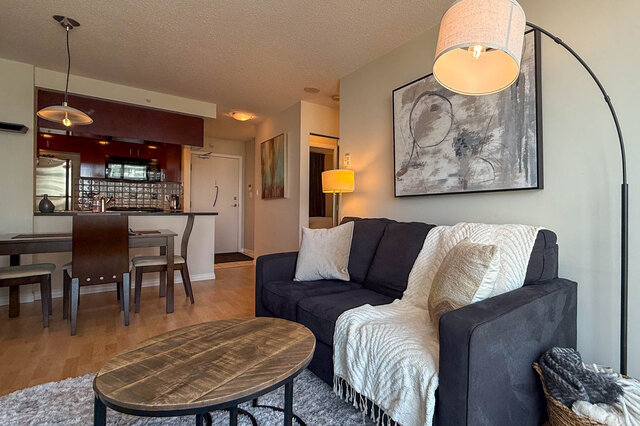 Spacious living room with modern decor, featuring a dark gray sofa, wooden coffee table, and a large abstract wall art piece.