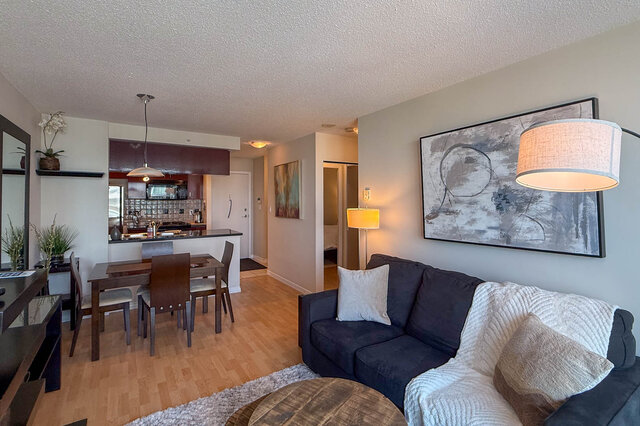 Spacious living room with modern art and cozy furnishings, featuring hardwood floors and a kitchen in the background.
