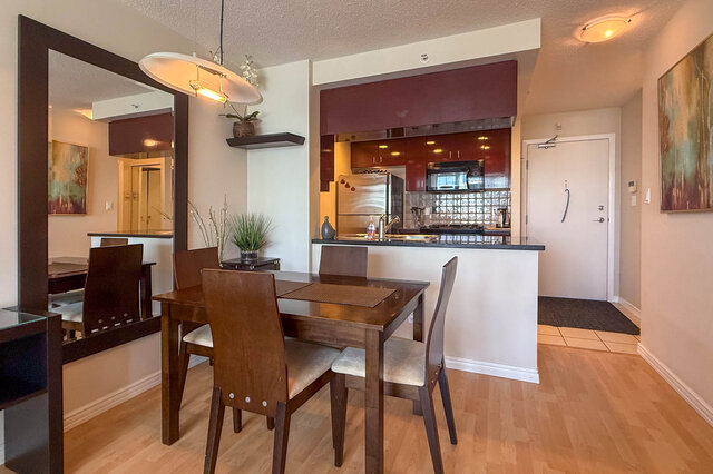 Open-concept dining and kitchen area with hardwood floors, modern decor, and a glass block backsplash.
