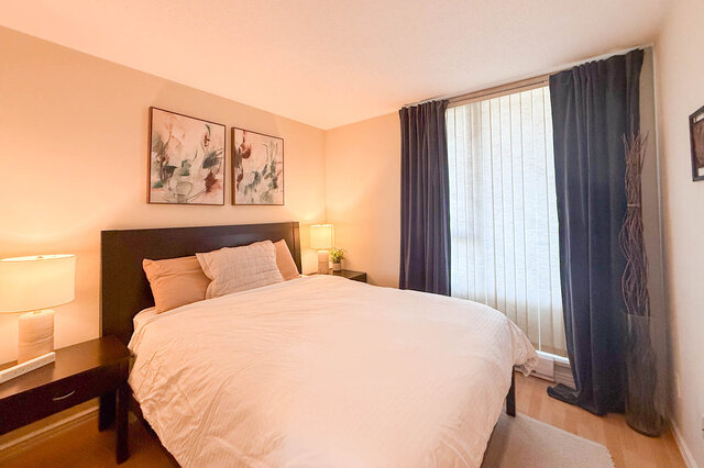 Spacious 1-bedroom condo with modern decor, featuring a cozy bed, stylish artwork, and a large window with blinds.