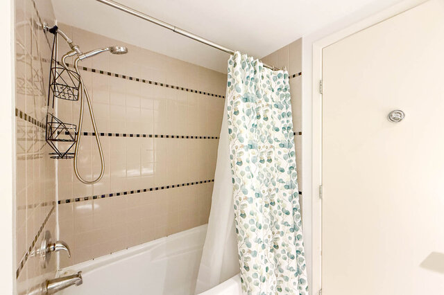Spacious bathroom with white tiles, a shower curtain with green leaf pattern, and a modern showerhead.