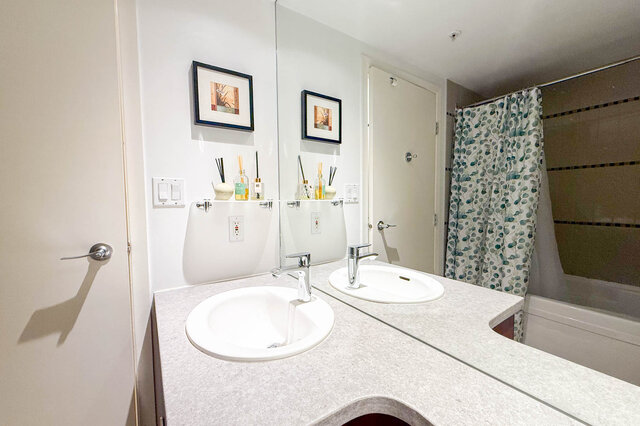 Spacious bathroom with dual sinks, granite countertops, and a shower with a patterned curtain. - 2602 - 1033 Marinaside Crescent, Vancouver Downtown