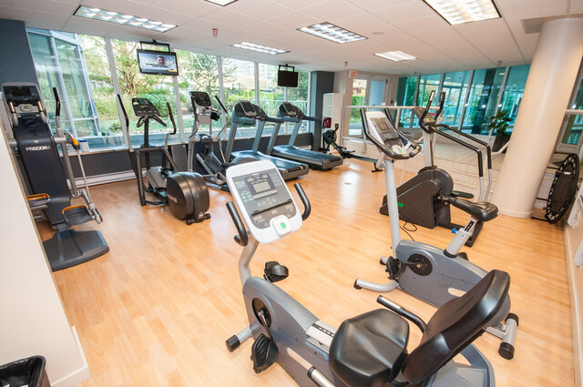 Spacious fitness room with hardwood floors, cardio machines, and large windows offering a city view.