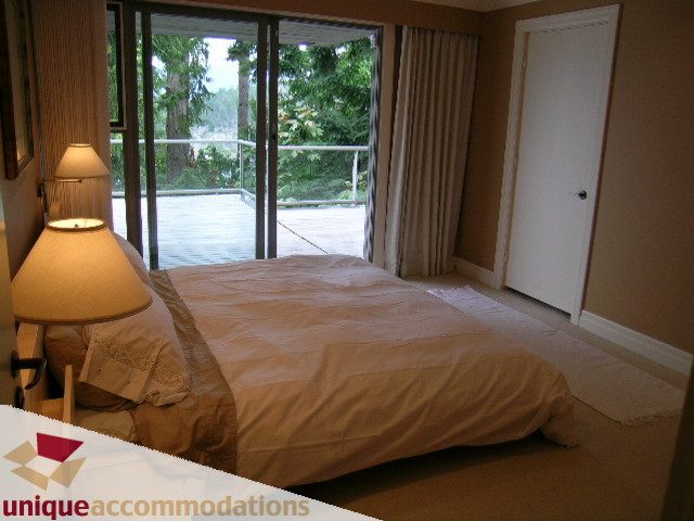 Spacious bedroom with large windows, view of trees and deck, neatly made bed. - 6189 Nelson Avenue, West Vancouver
