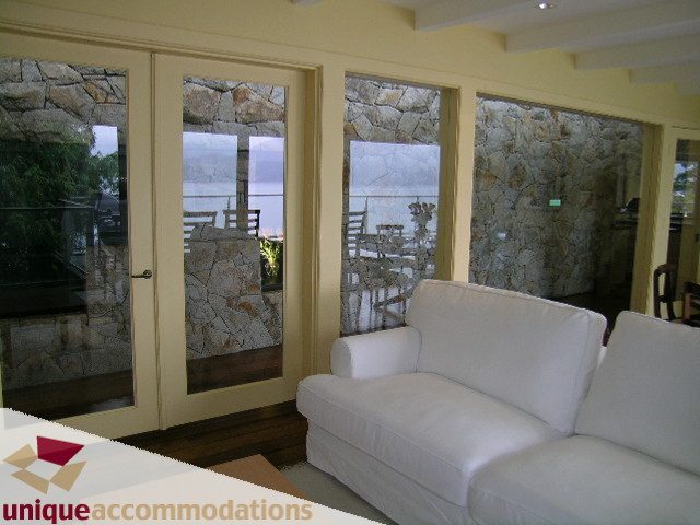 Furnished living room with stone walls and large windows offering a scenic view. - 6189 Nelson Avenue, West Vancouver
