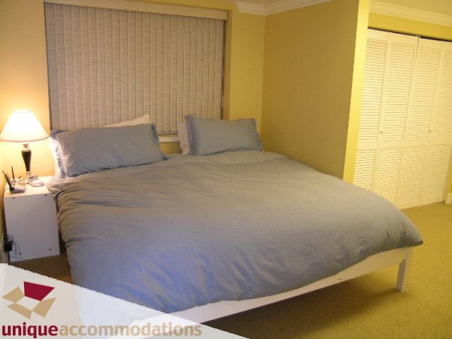 Furnished bedroom with a modern bed, light yellow walls, and a bedside lamp. - 6189 Nelson Avenue, West Vancouver