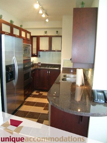 Bright kitchen with dark wood cabinets, granite countertops, and stainless steel appliances. - 302 - 1228 West Hastings Street, Vancouver Downtown
