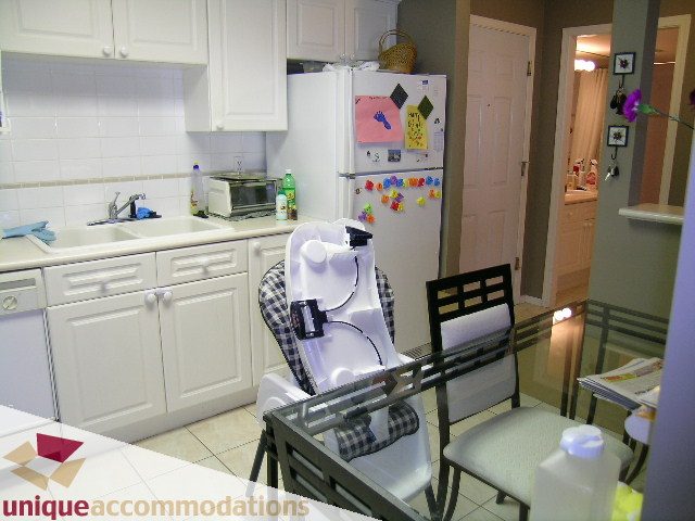 Bright kitchen with white cabinets, tiled backsplash, and a cozy dining area with checkered chairs. - 314 - 855 W. 16th Street, North Vancouver
