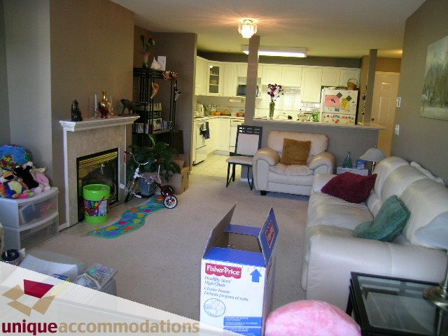 Furnished living room with beige couches, kitchen counter, and fireplace. - 314 - 855 W. 16th Street, North Vancouver